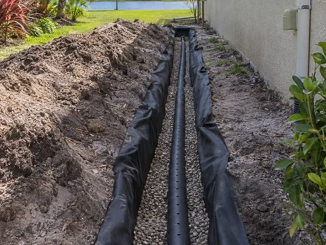 Open trench with drainage pipe and excavated soil beside a building