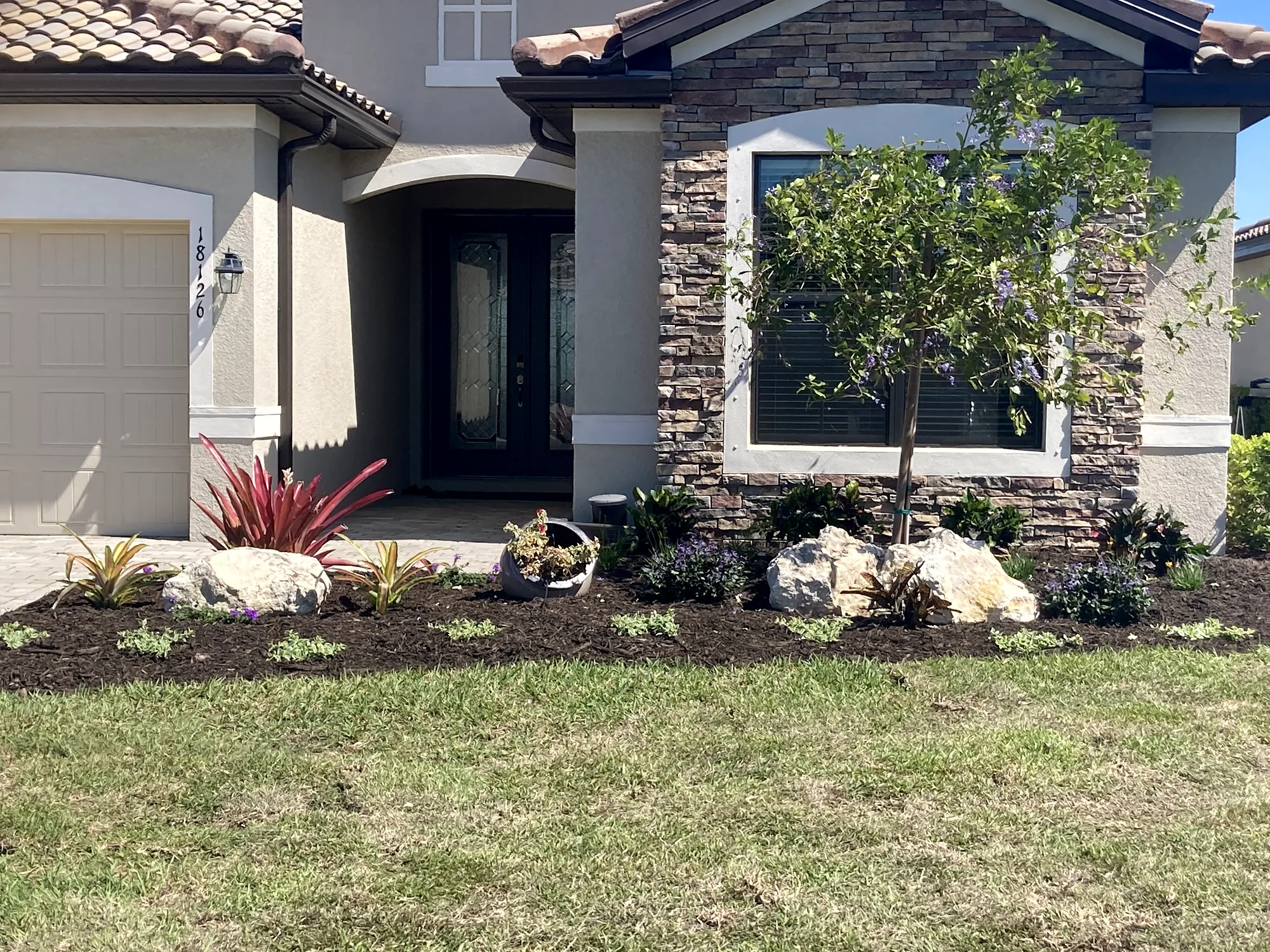 House entrance with a small tree, shrubs, rock and mulch beds beside a lawn