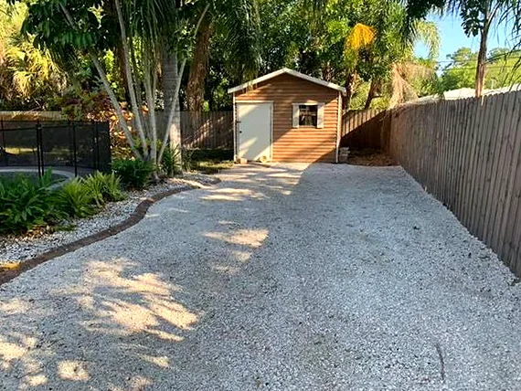 Shell gravel driveway running along a wood fence to a backyard shed