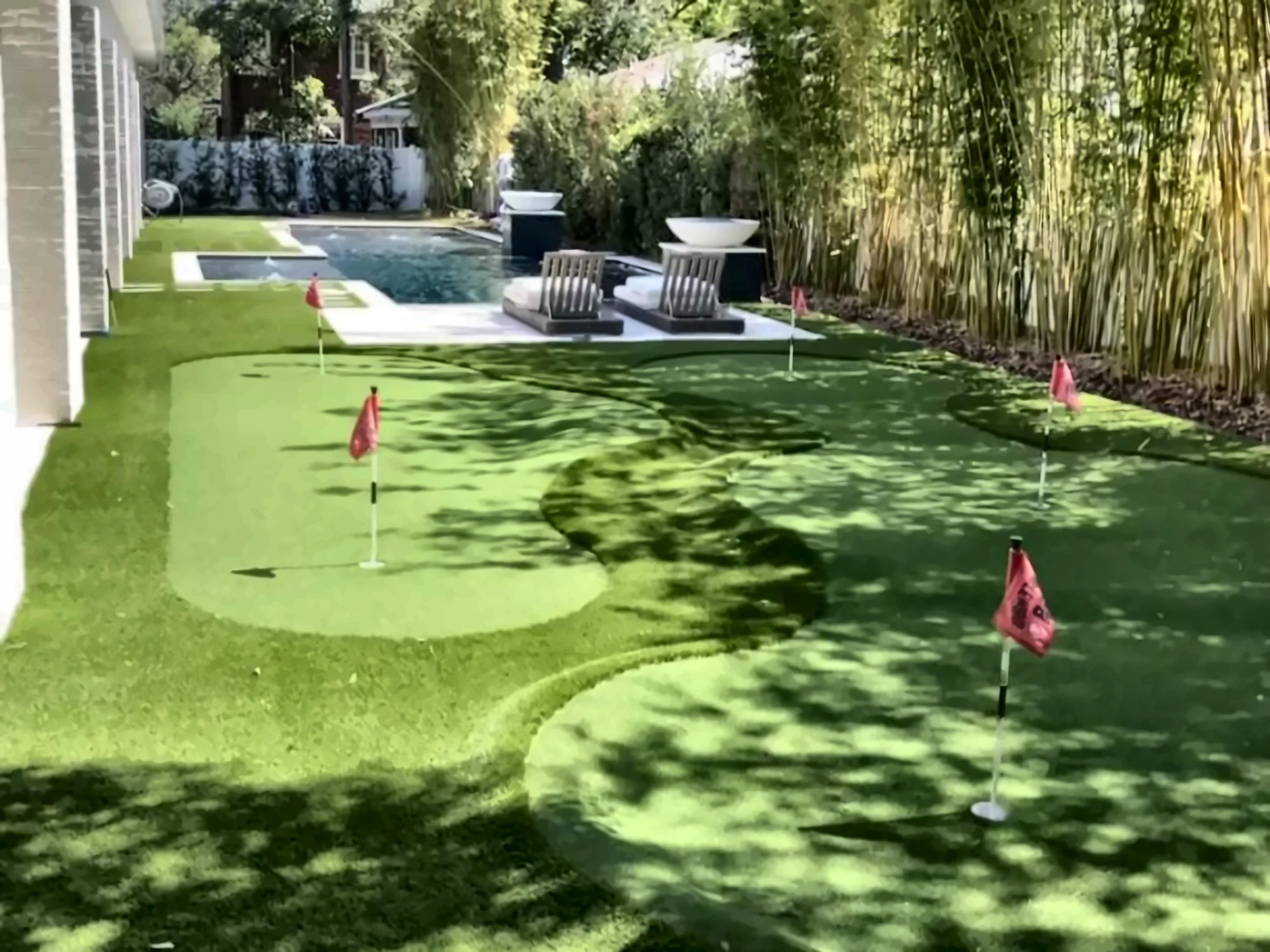 Artificial turf putting green with pin flags beside a backyard pool