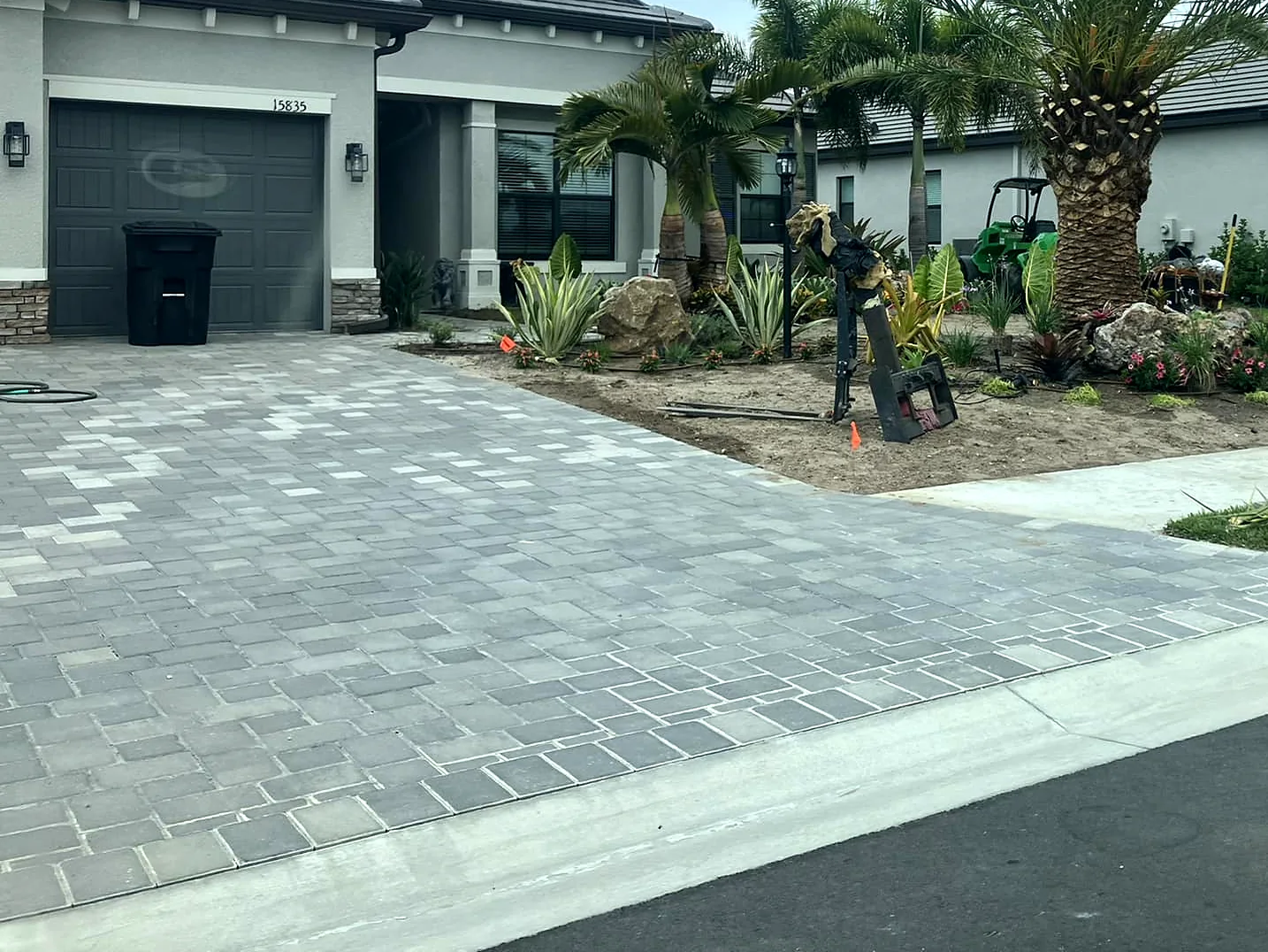 New paver driveway with palms and planting beds at a single-story home