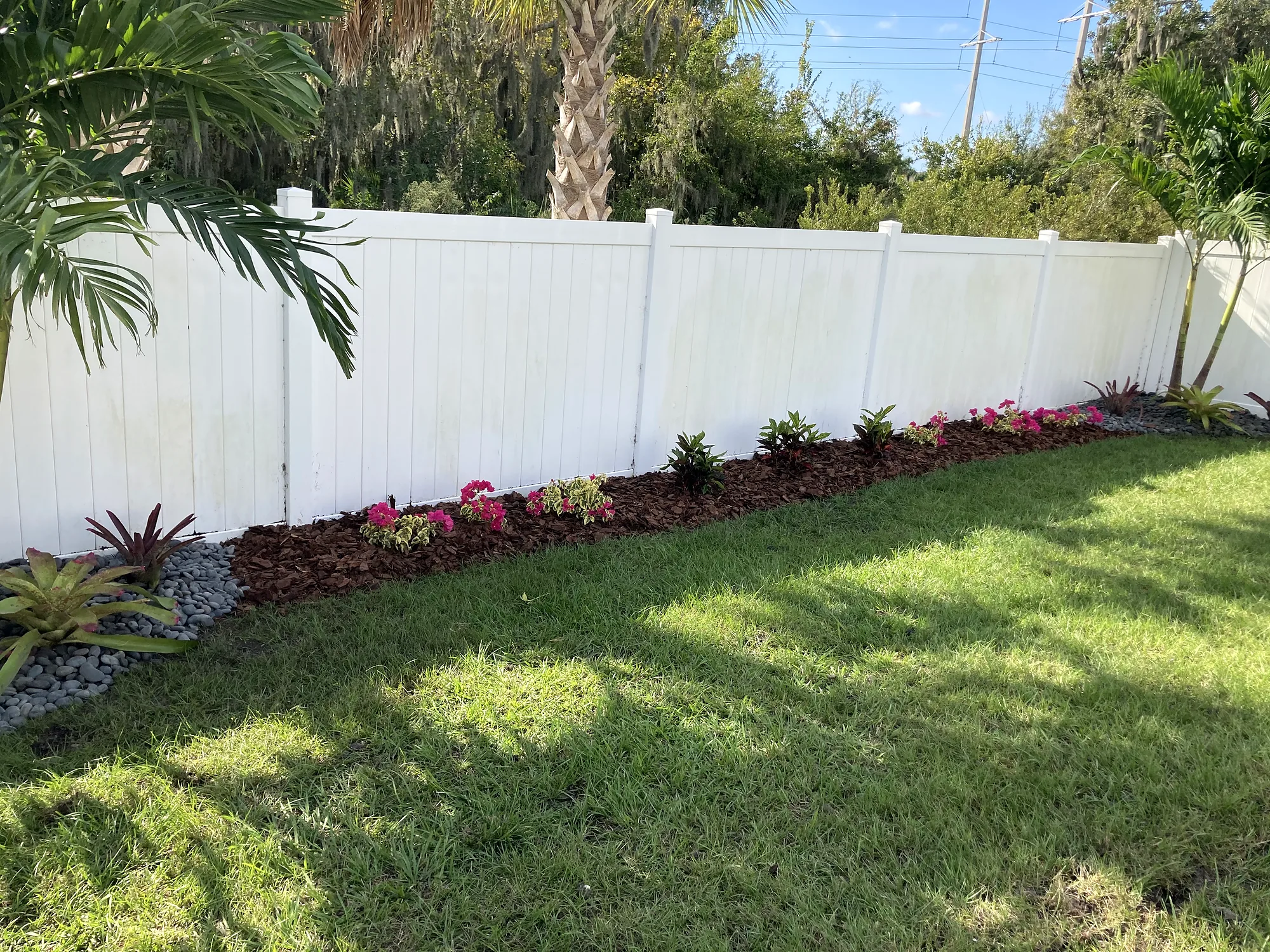 Long planting bed with flowering plants along a white vinyl fence