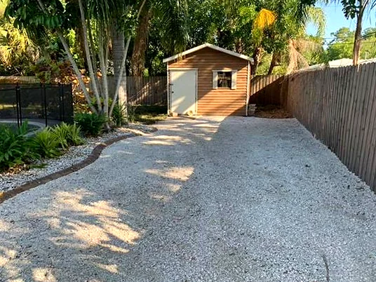 Gravel driveway running along a wood fence to a backyard shed